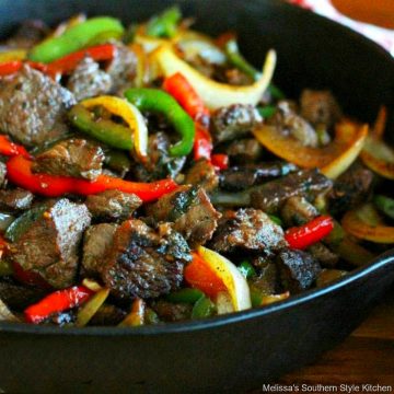 black skillet with sirloin tips, red, green and yellow bell peppers and onions
