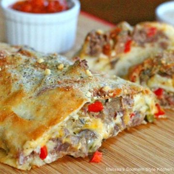Sliced pepper steak stromboli on a cutting board with pizza sauce