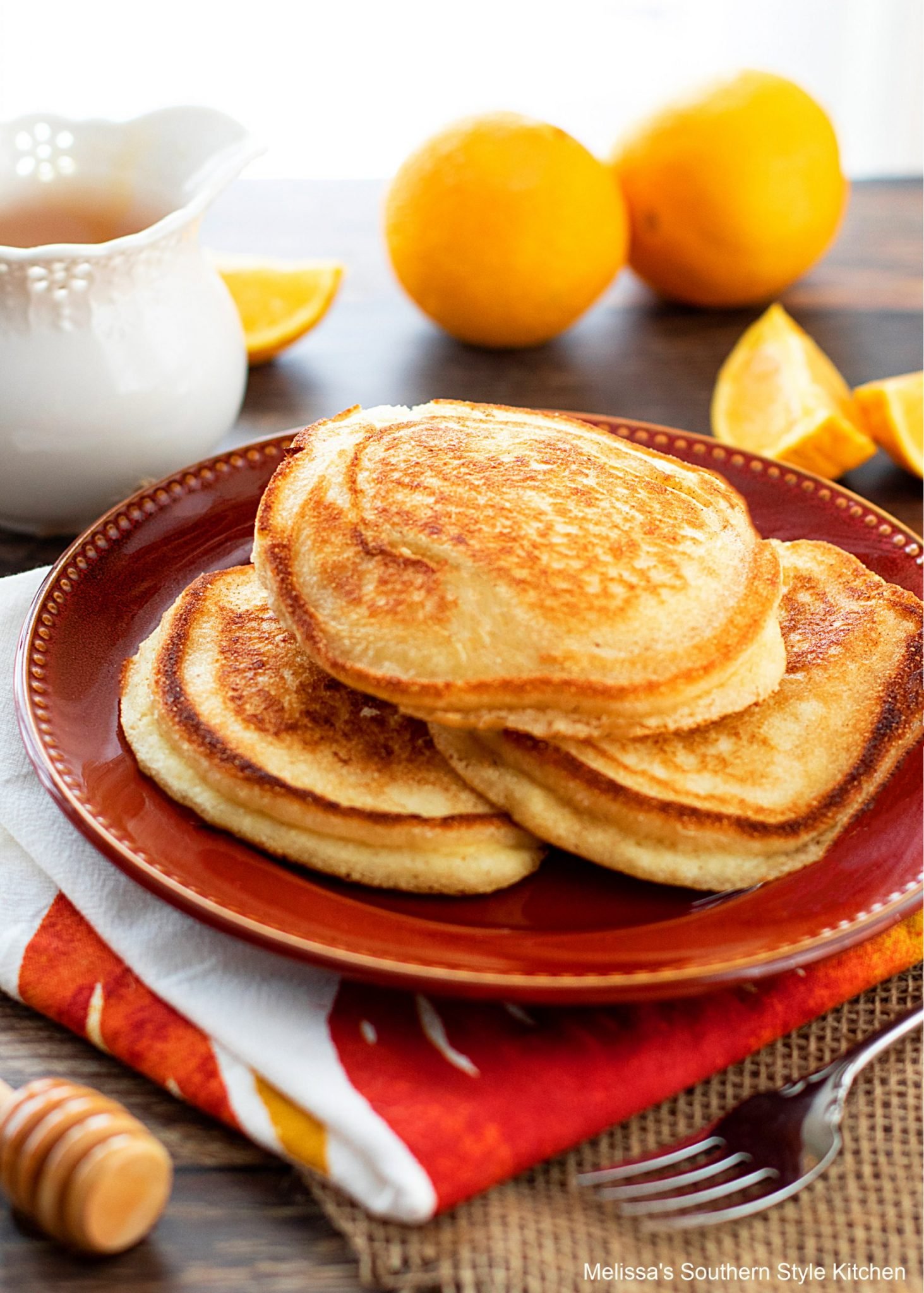 cooked johnnycakes on a red plate with orange wedges and a fork