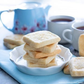 square shortbread cookies on a white plate with a blue tea pot and white tea cups
